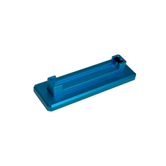 A bright blue anodized aluminum rectangular block with a recessed channel and small protruding tabs, photographed on a round off-white platform against a white background.