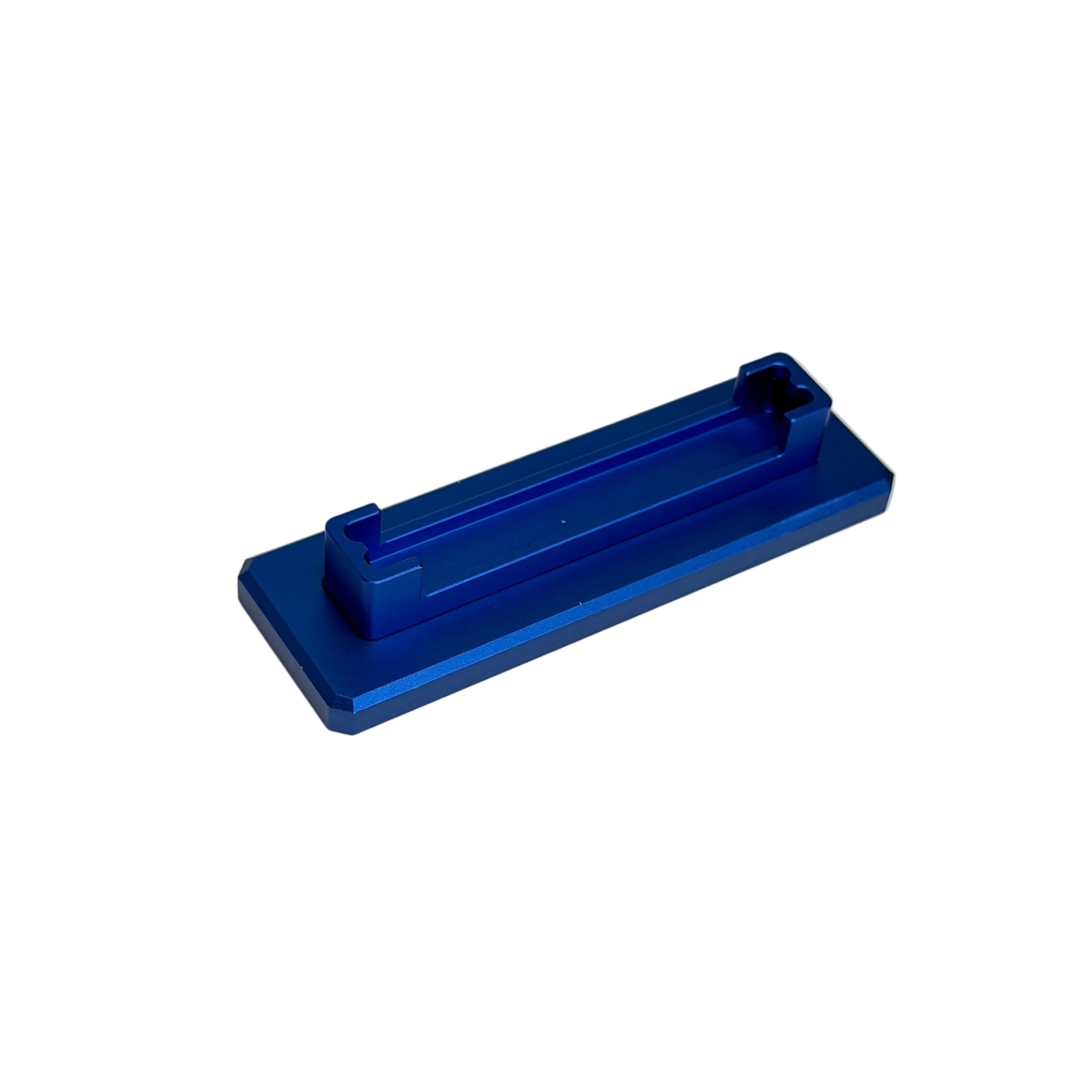 A small metallic blue rectangular tool or accessory with a recessed channel, placed on a round off-white display surface against a white background.