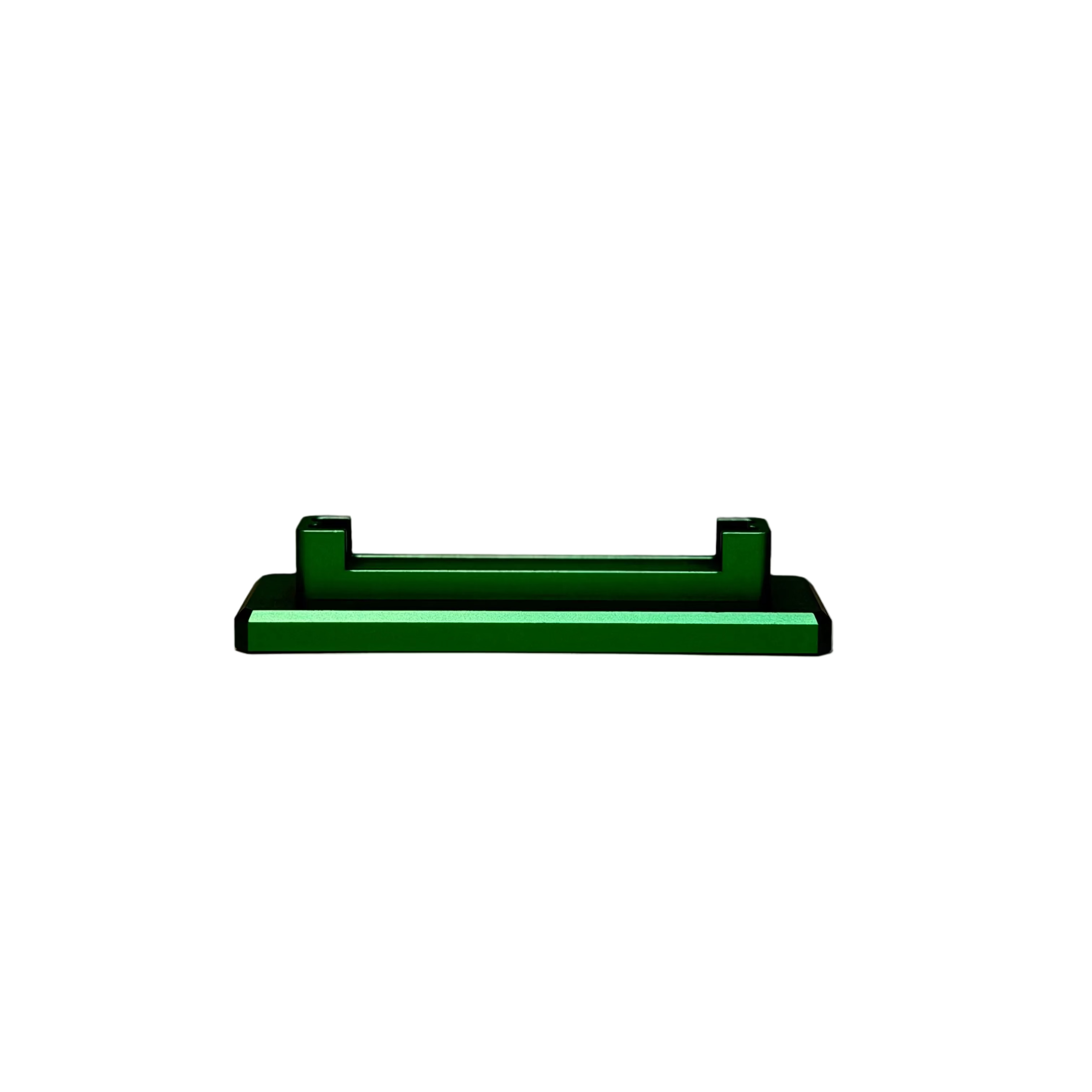 A small dark green rectangular metal component with two raised tabs, displayed on a round off-white pedestal against a textured light beige background.