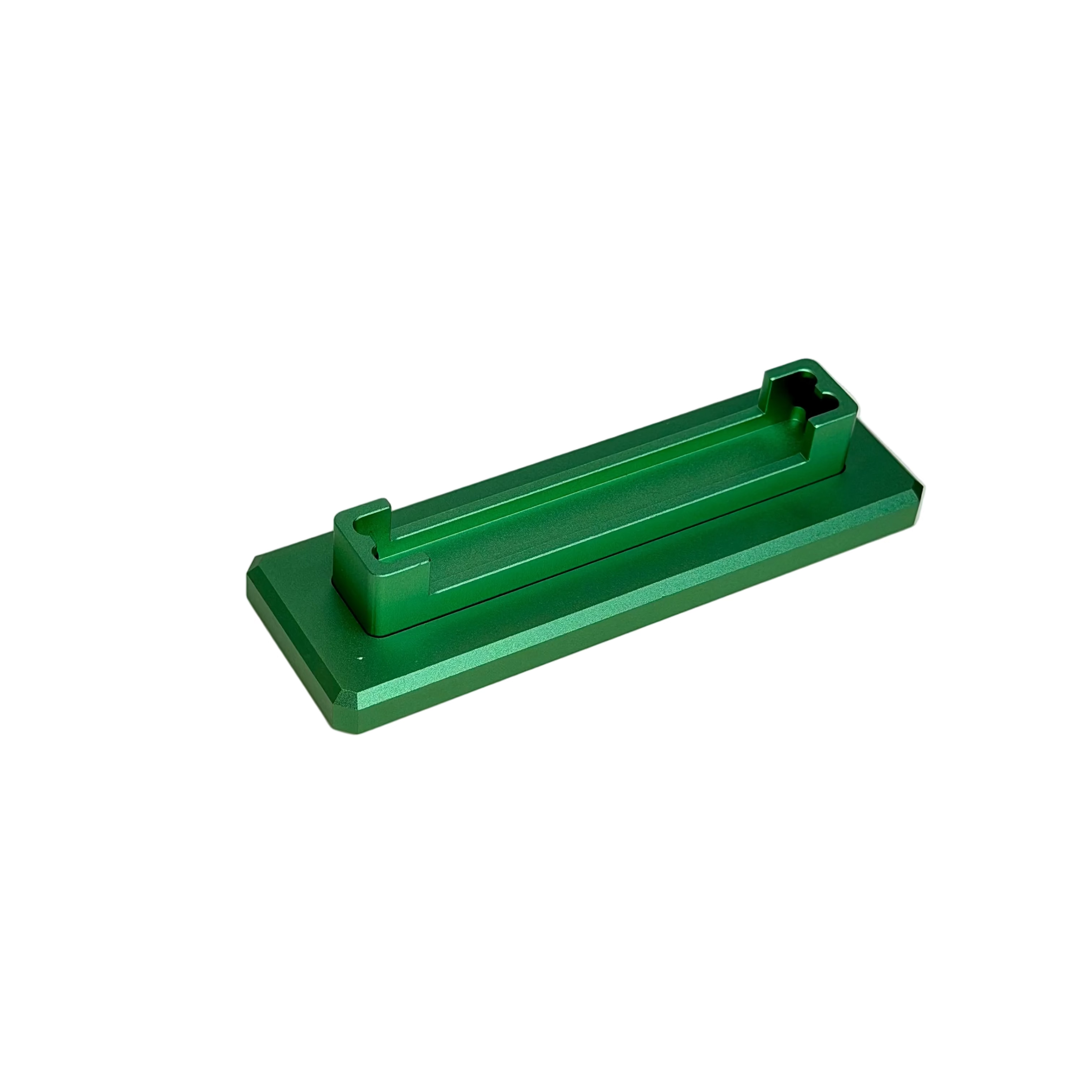 A small green anodized metal component with a rectangular base and a raised channel, displayed on a round off-white ceramic turntable.