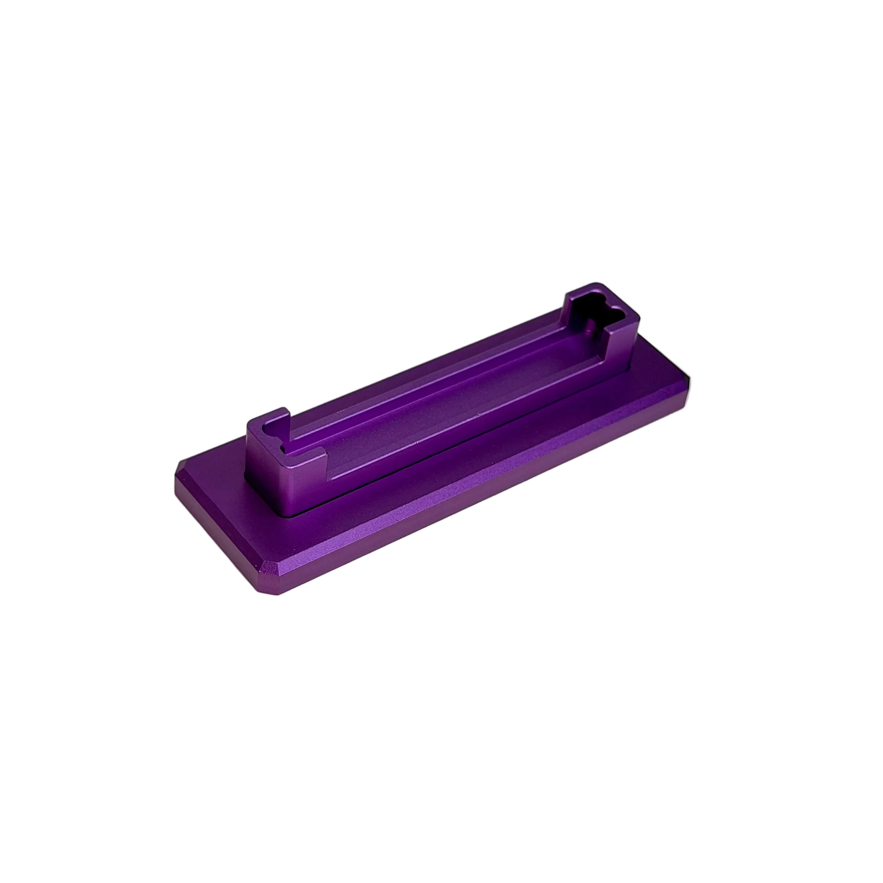 A small metallic purple rectangular component with a raised central ridge, photographed on a round off-white platform against a white background.